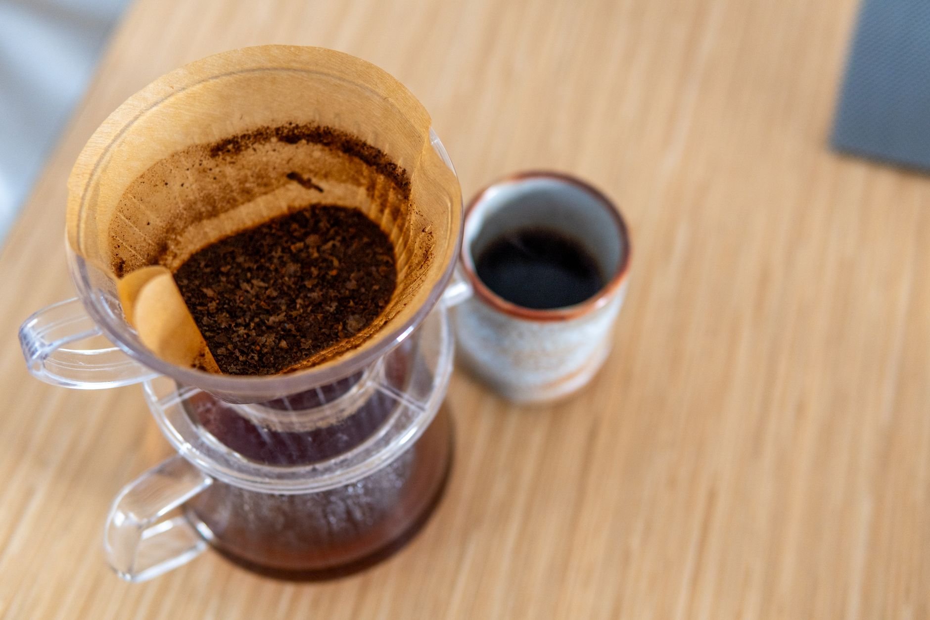 Top-down view of pour-over coffee in a filter next to a ceramic mug on a wooden table