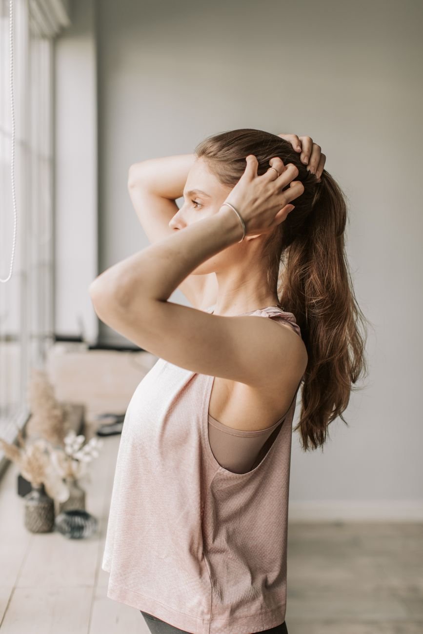Side view of a woman tying her hair in a sunlit minimalist room