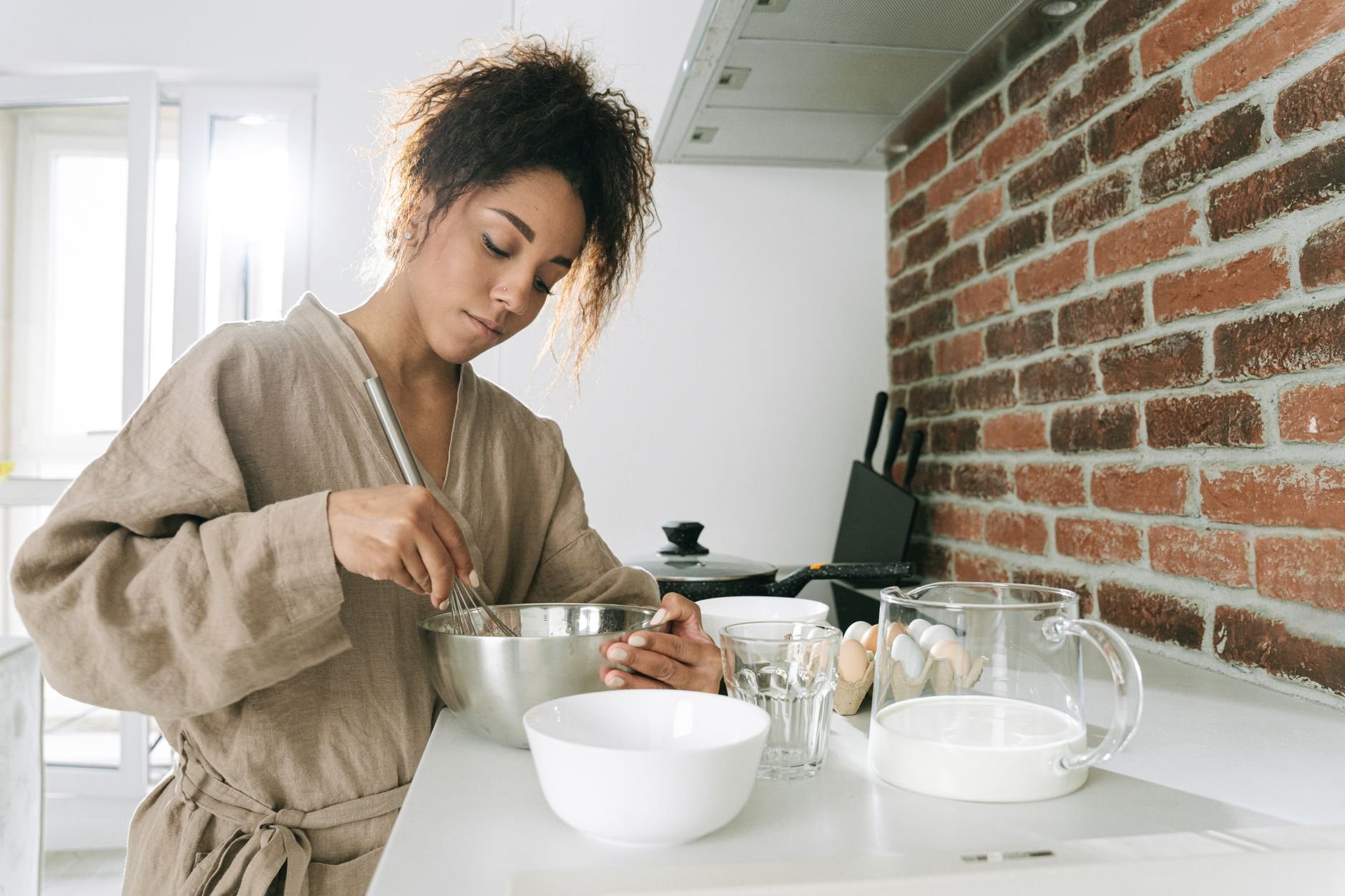 A woman in a contemporary kitchen surrounded by botanical ingredients and morning wellness products
